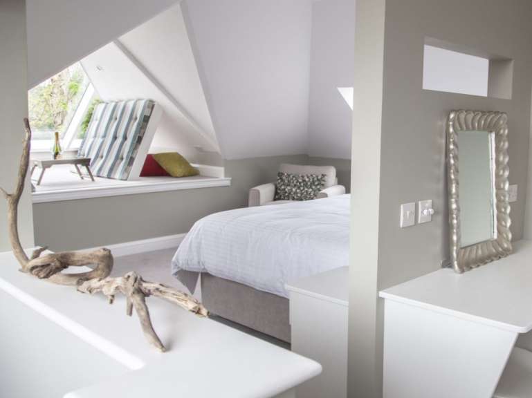 Ein stilvolles Schlafzimmer mit einem Bett, einem Sessel und einem Fenster, das einen Blick nach draußen freigibt.
