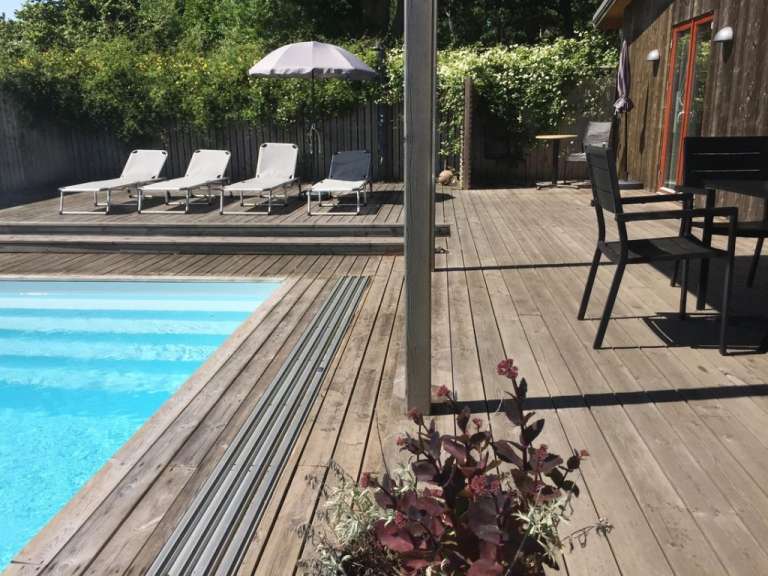 Liegestühle stehen auf einem Holzdeck neben einem Swimmingpool