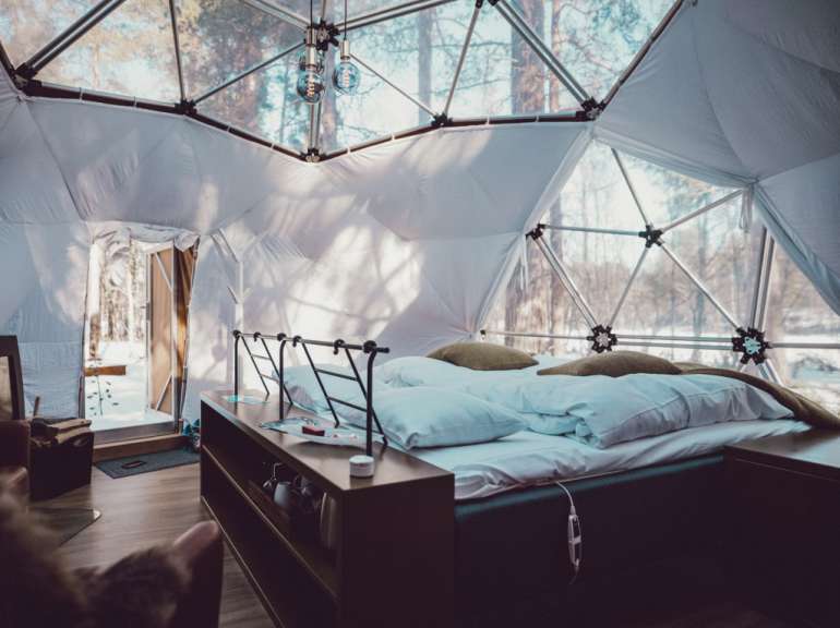 Ein Bett in einem weißen Zelt mit Blick auf den Wald