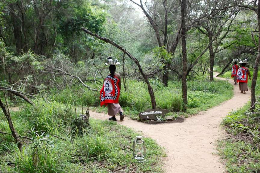 Eine Gruppe von Frauen geht auf einem Pfad in einem Wald mit einem Schild, das swanawana sagt