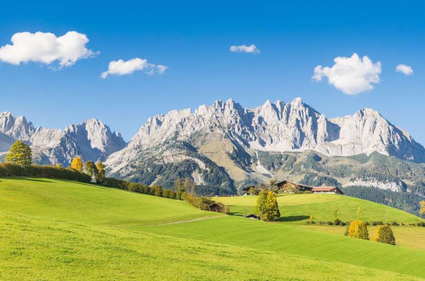 Ein Häuschen auf einem grünen Hügel mit Bergen im Hintergrund