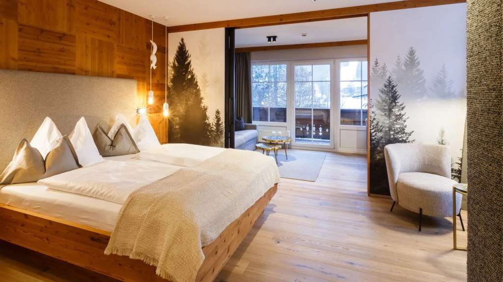 Dieses Bild zeigt ein Schlafzimmer mit einem Holzbett, einem Wandgemälde von Bäumen und einer Glasfront, die den Blick auf die Natur freigibt.