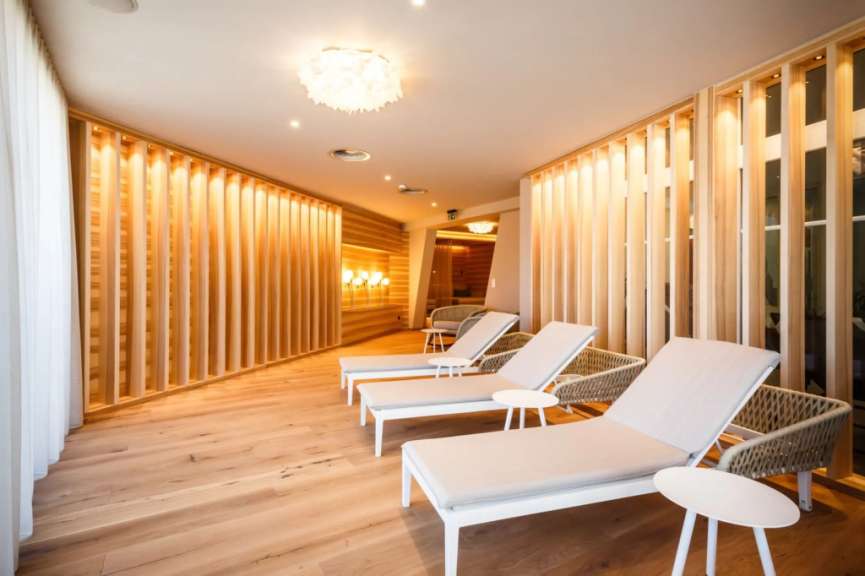 In einem modernen Wellnessbereich stehen mehrere Liegen auf einem Holzboden vor einer mit Holzlamellen verkleideten Wand.