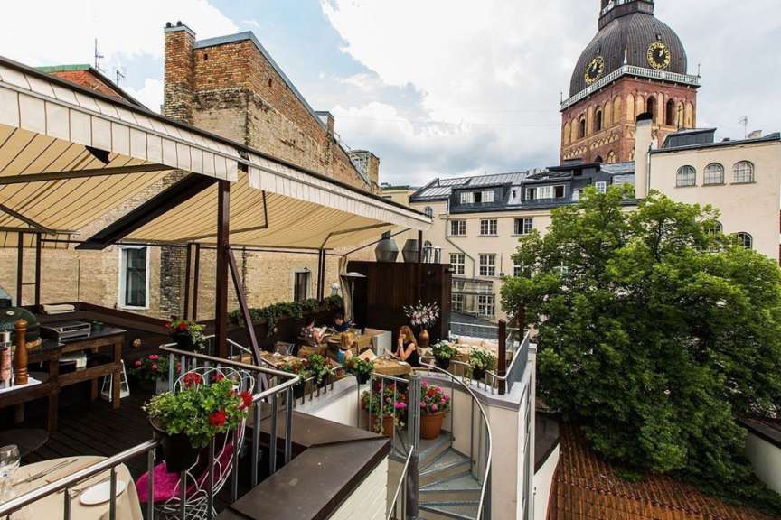 Eine Gruppe von Menschen sitzt auf einem Balkon mit einem Uhrturm im Hintergrund