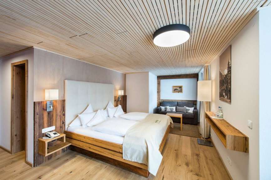 Dieses Bild zeigt ein geräumiges Hotelzimmer mit einem Doppelbett, einem Sofa und einem Holzboden, das in einem rustikalen, aber modernen Stil eingerichtet ist.