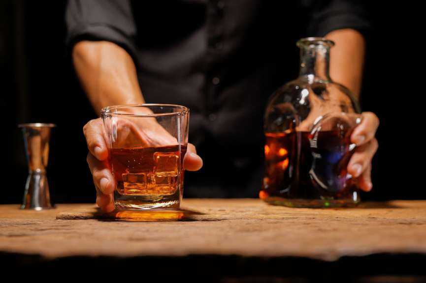 Eine Person hält ein Glas Whiskey mit Eiswürfeln