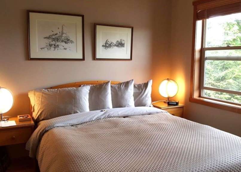 Ein Schlafzimmer mit einem Bett, zwei Nachttischen, zwei gerahmten Bildern und einem Fenster.
