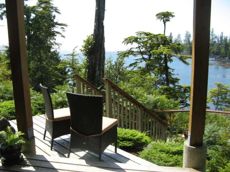 Zwei Stühle stehen auf einer Holzterrasse mit Blick auf das Meer und üppige Vegetation.