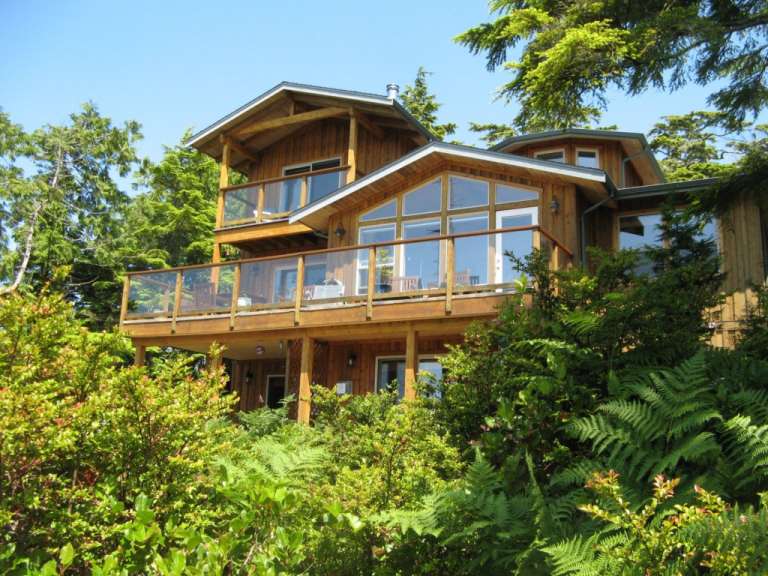 Ein holzverkleidetes Haus mit mehreren Ebenen und großen Fenstern ist von üppigem Grün umgeben.