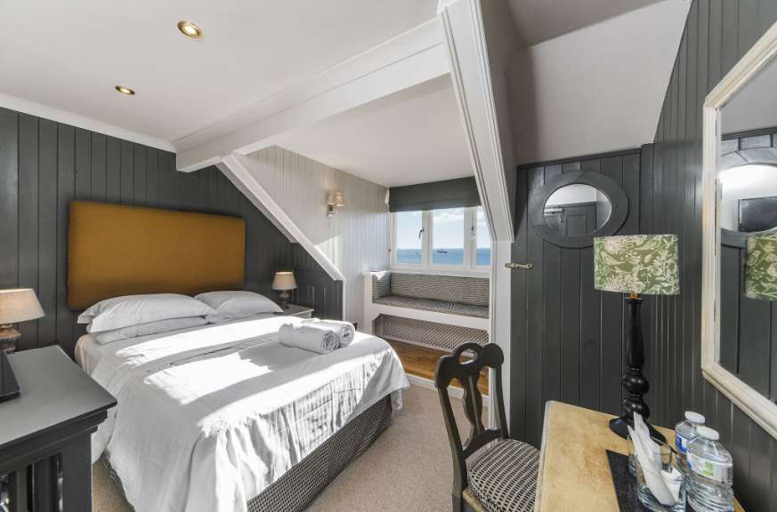 Ein Schlafzimmer mit einem Bett, einem Fenster mit Blick aufs Meer und einem Schreibtisch ist in dieser Aufnahme zu sehen.
