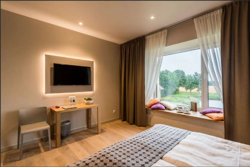 Ein modern eingerichtetes Hotelzimmer mit einem Bett, einem Schreibtisch, einem Fernseher und einem großen Fenster mit Blick auf die Natur.