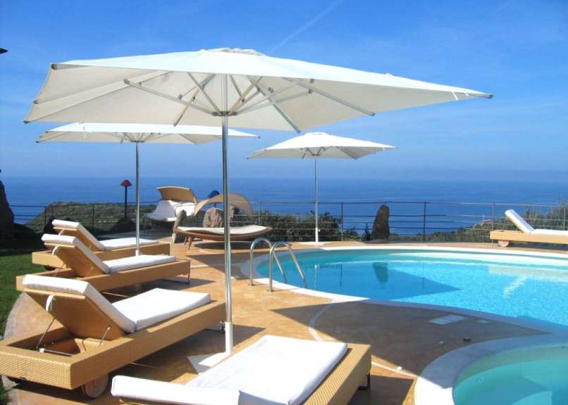 Liegestühle und Sonnenschirme um einen Pool mit Blick auf das Meer