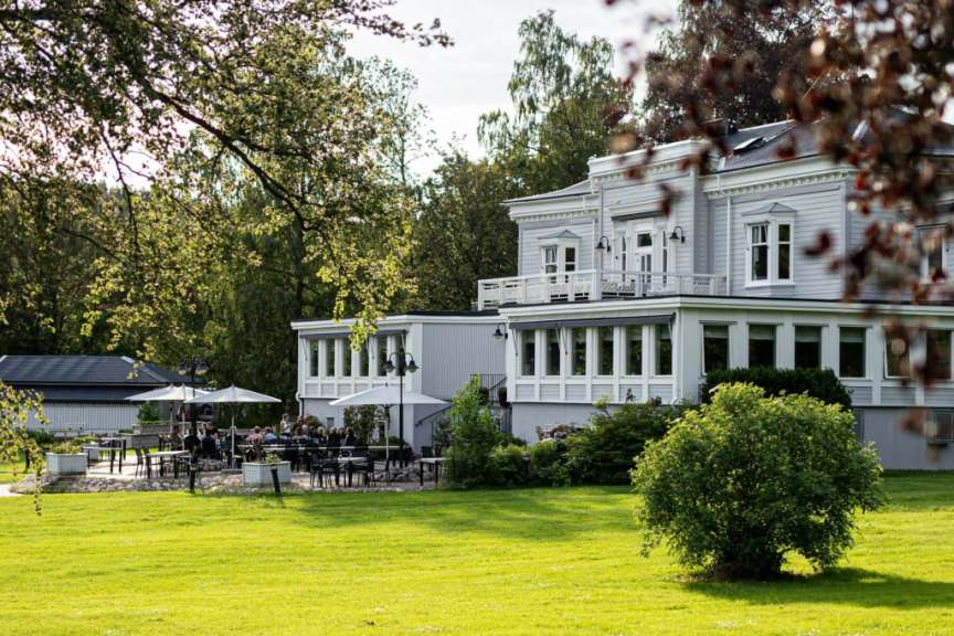Eine Gruppe von Menschen sitzt auf einer Terrasse vor einem großen weißen Gebäude