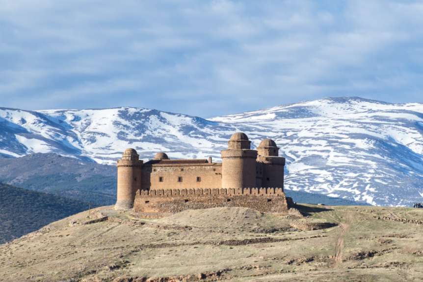 Eine Burg auf einem Hügel mit schneebedeckten Bergen im Hintergrund
