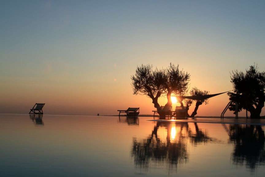 Sonnenuntergang über einem Infinity-Pool mit Liegestühlen und Bäumen