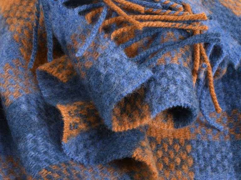Eine Nahaufnahme einer blauen und orangefarbenen Decke mit Fransen