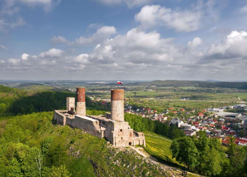 Eine Burgruine auf einem Hügel, mit einem Dorf im Hintergrund und bewölktem Himmel.