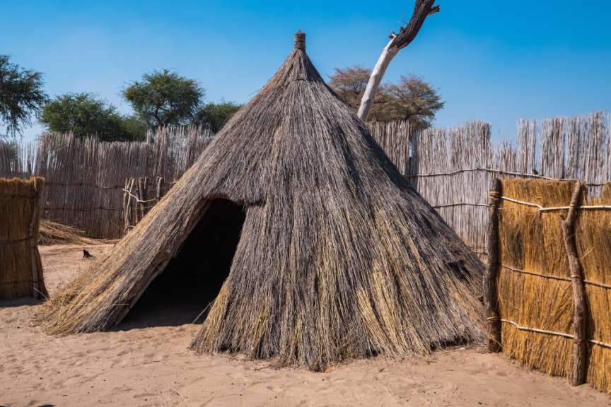 Ein Zelt aus Stroh steht im Sand neben einem Zaun