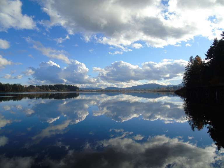 Ein See mit Bergen im Hintergrund und Wolken im Wasser