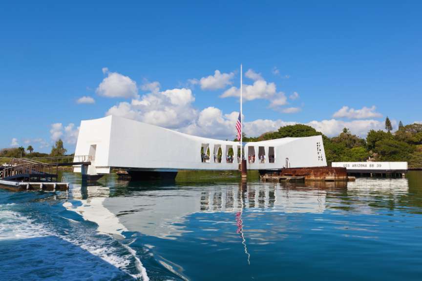 Ein Boot fährt vor einem weißen Gebäude mit der Aufschrift uss arizona