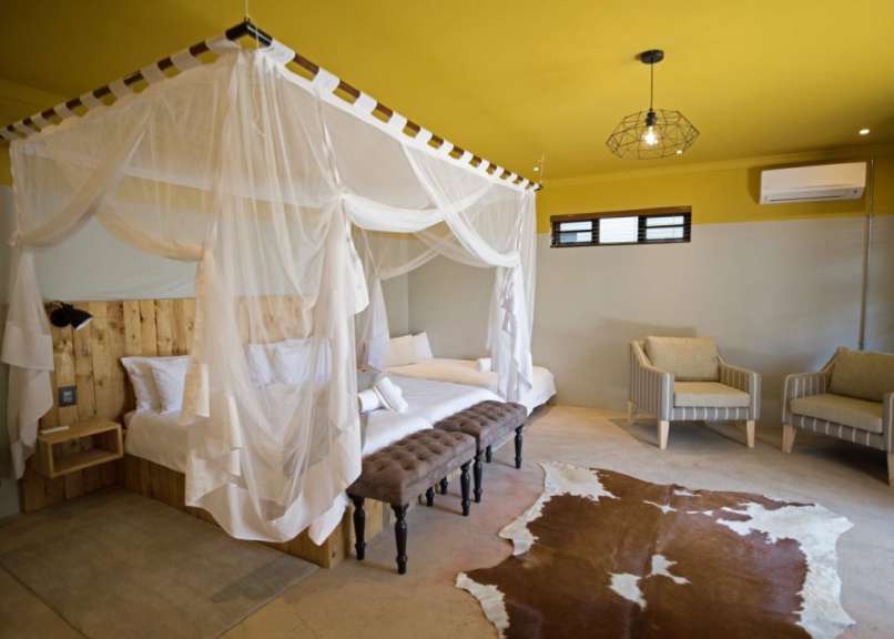 Ein Schlafzimmer mit Himmelbetten und beigen Sesseln ist mit einer Kuhhaut und einer gelben Decke geschmückt.