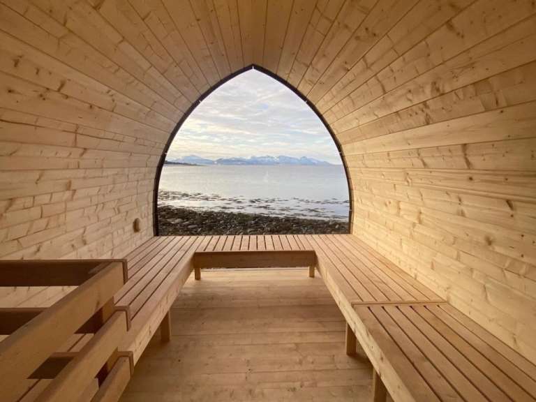 Eine Holzsauna mit Bänken und einem Fenster mit Blick auf den Ozean