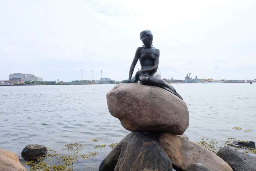Eine Statue einer Meerjungfrau sitzt auf einem Felsen im Wasser