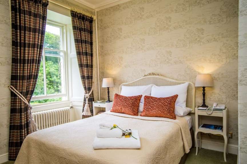 Ein Schlafzimmer mit einem großen Bett, zwei Nachttischen, einer Lampe und einem Fenster mit Gardinen wird auf diesem Bild gezeigt.