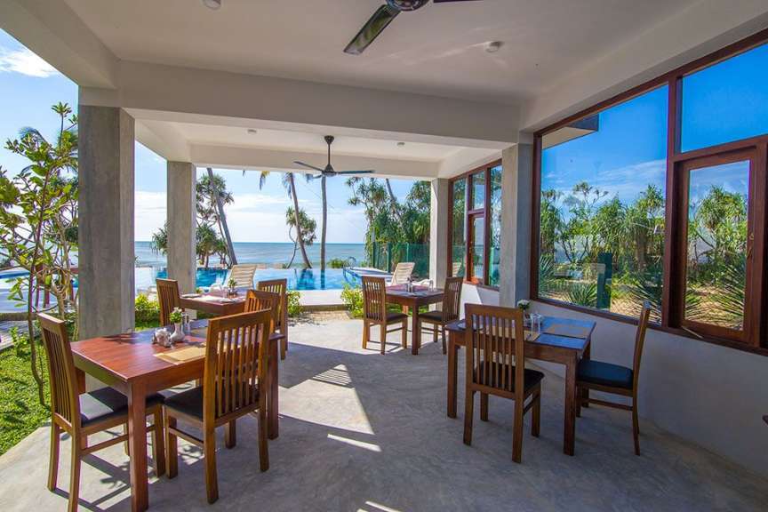 Ein überdachter Essbereich mit Holztischen und Stühlen blickt auf einen Infinity-Pool und das Meer.