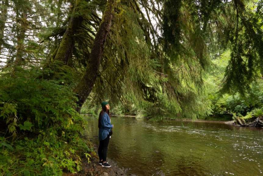 Eine Frau steht neben einem Fluss in einem Wald