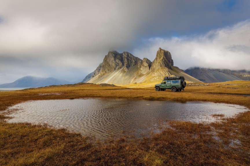 Ein grüner jeep steht neben einem kleinen teich mit einem berg im hintergrund