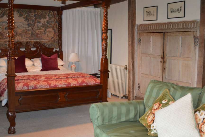 Ein Himmelbett mit einer roten Tagesdecke steht in einem Zimmer mit Wandbehängen und einer grünen Couch.