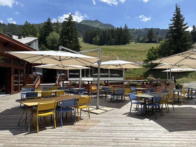 Eine Terrasse mit Tischen und Stühlen und Sonnenschirmen mit einem Berg im Hintergrund