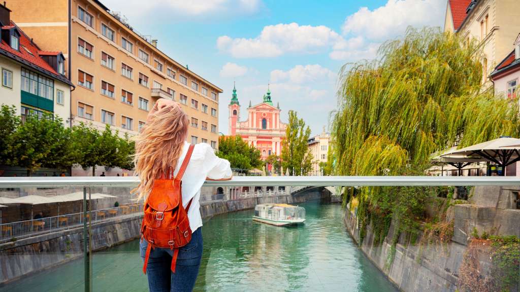 Eine Frau mit einem roten Rucksack steht auf einer Brücke über einen Fluss