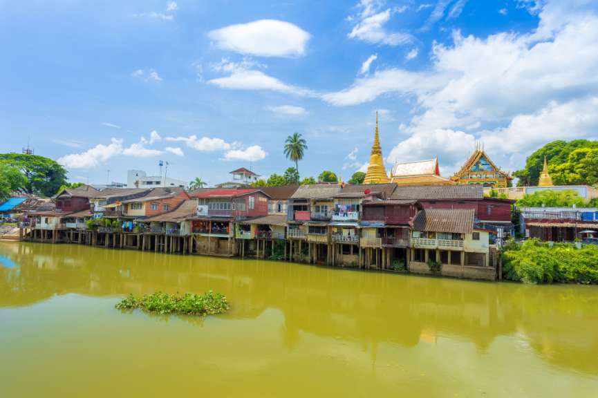 Eine Reihe von Häusern neben einem Fluss mit einem goldenen Pagode im Hintergrund