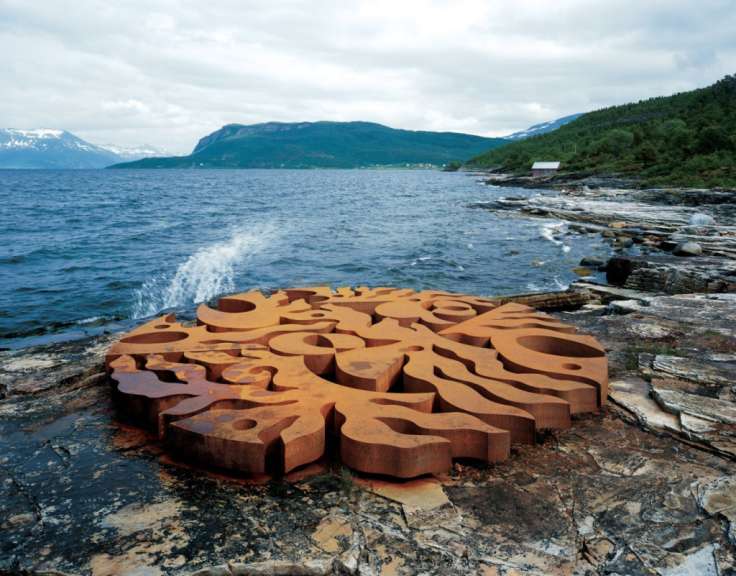 Eine große Metallskulptur steht auf einem Felsen in der Nähe eines Sees