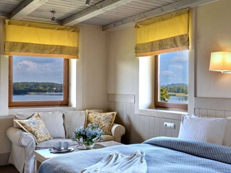 Ein Zimmer mit einem Bett, einem Couchtisch und zwei Fenstern mit Blick auf einen See