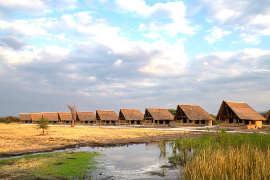 Eine Reihe strohgedeckter Häuser steht neben einem Teich