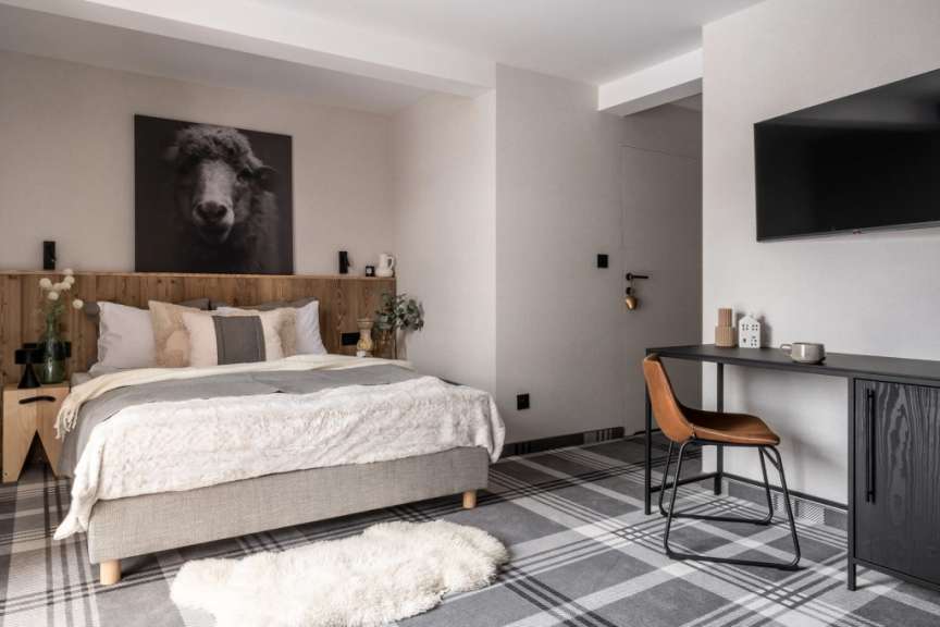 Ein modernes Schlafzimmer mit einem schlichten Doppelbett, einem Schreibtisch und einem Fernsehgerät über dem Schreibtisch.