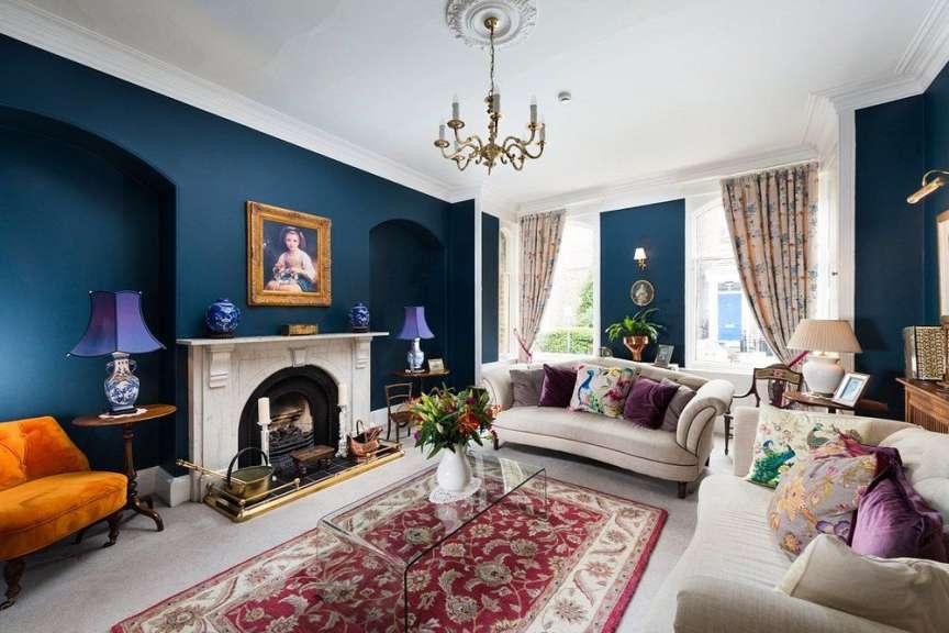 In einem stilvollen Wohnzimmer mit tiefblauen Wänden stehen zwei Sofas, ein Couchtisch, ein Kamin und ein Teppich.