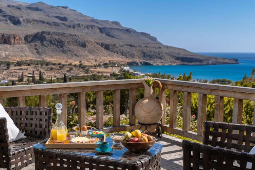 Ein Tisch mit einem Tablett mit Essen und Getränken auf einem Balkon mit Blick auf den Ozean