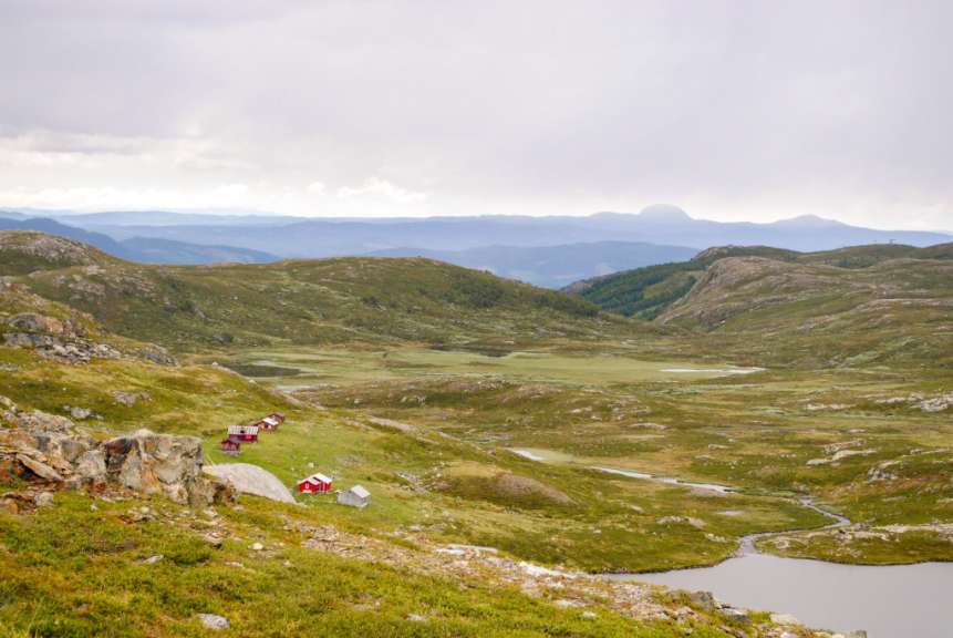 Eine bergige Landschaft mit kleinen roten Häusern und einem Fluss unter einem bewölkten Himmel.