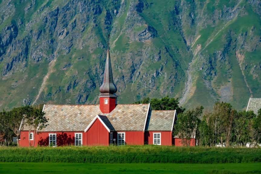 Eine kleine rote Kirche steht in einem grünen Feld vor einem Berg