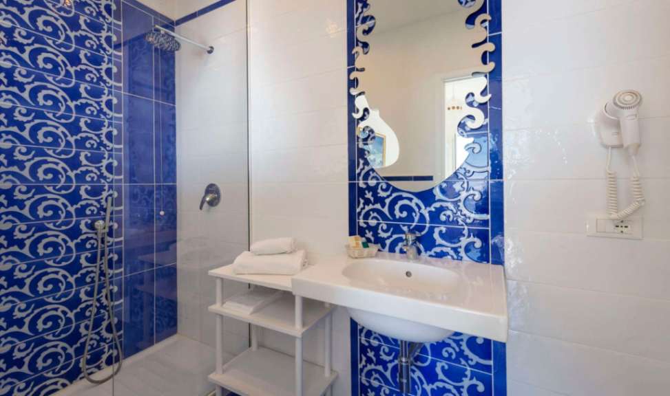 Ein Badezimmer mit blauen und weißen Fliesen, einer Dusche, einem Waschbecken und einem Haartrockner.