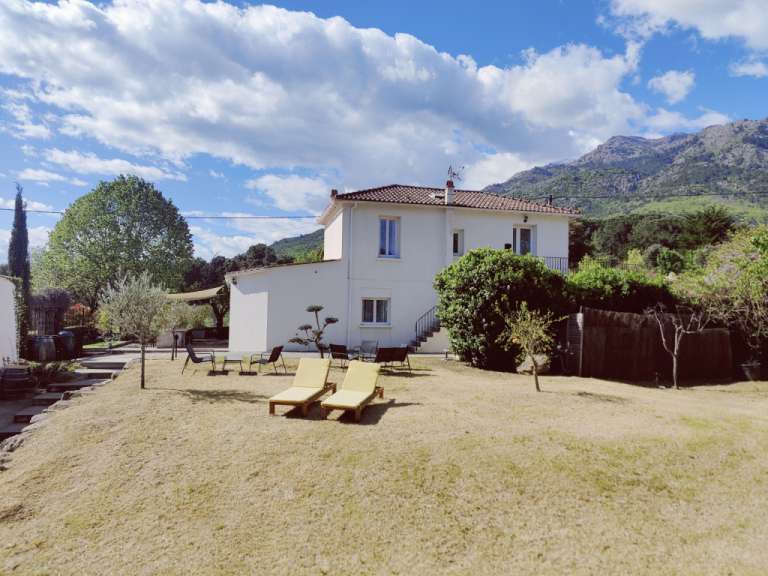 Ein weißes Haus mit einem roten Dach und einem Tisch und Stühlen im Garten