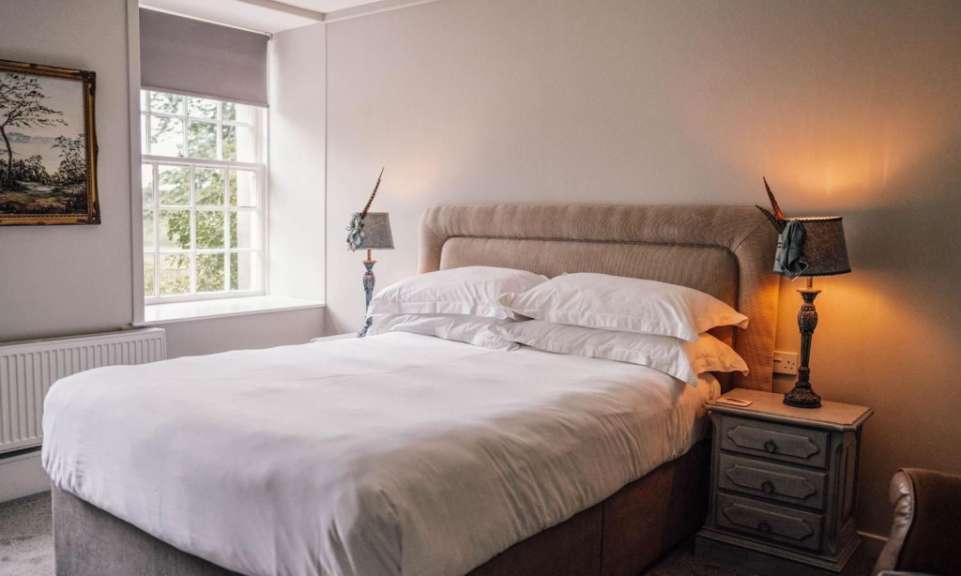 Ein Schlafzimmer mit einem großen Bett, zwei Nachttischlampen, einem Fenster und einem Gemälde.
