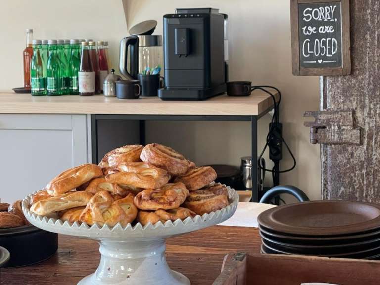Ein Berg von Gebäck liegt auf einer weißen Keramikschale vor einer Wand mit einem "Closed"-Schild und einem Kaffeeautomaten.