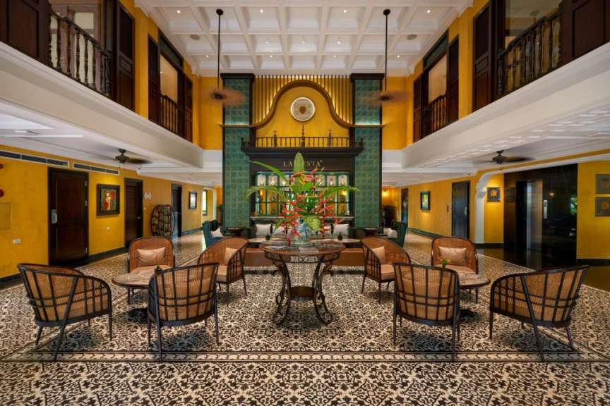 Ein Hotel-Foyer mit gelben Wänden, kunstvollen Fliesenböden und Sitzbereichen im Rattan-Stil.