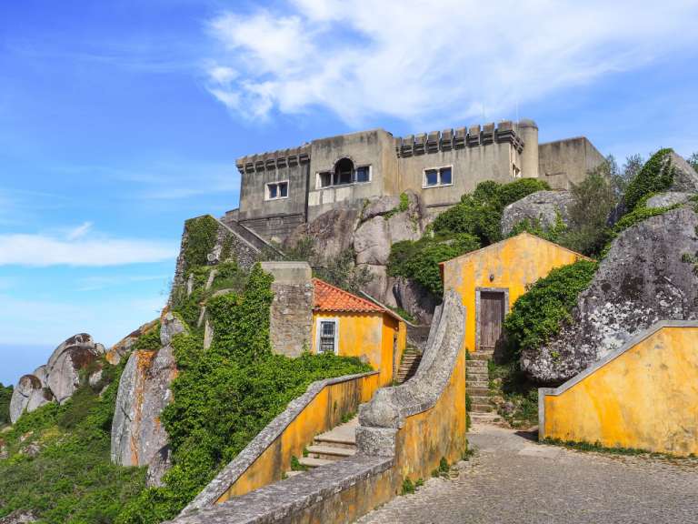 Ein gelbes Haus auf einem Hügel mit einem großen Gebäude dahinter