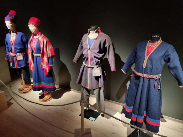 Auf einer Museumslichtung sind vier traditionelle Samischen Trachten, die auf Schaufensterpuppen drapiert sind, ausgestellt.